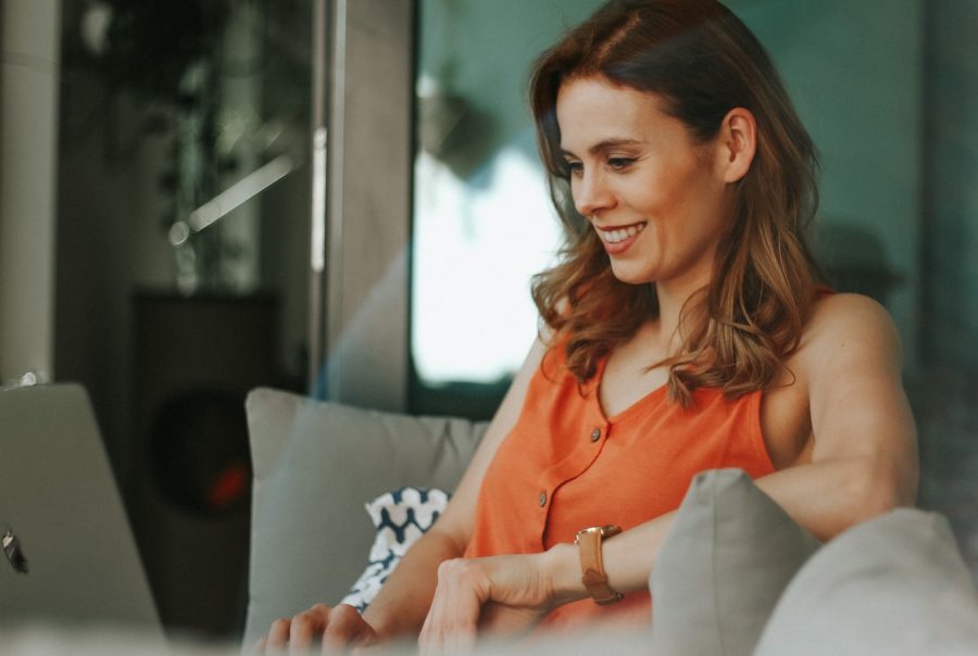 Vrouw in oranje top zit ontspannen op de zetel en leest een bericht op haar telefoon