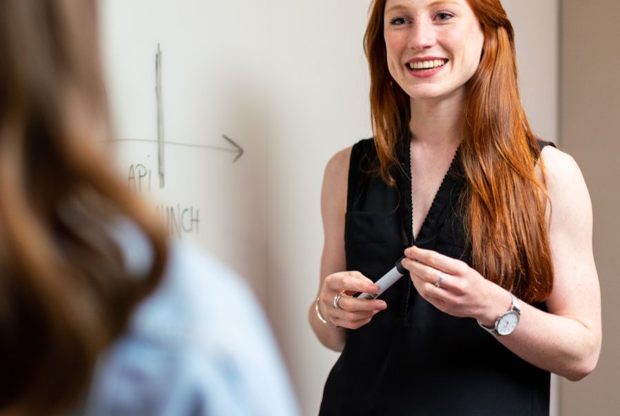Vrouw legt aan een whiteboard de planning uit aan een collega