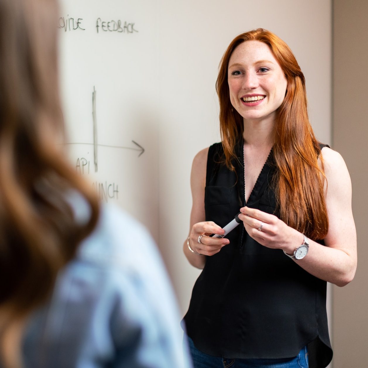 Vrouw legt aan een whiteboard de planning uit aan een collega