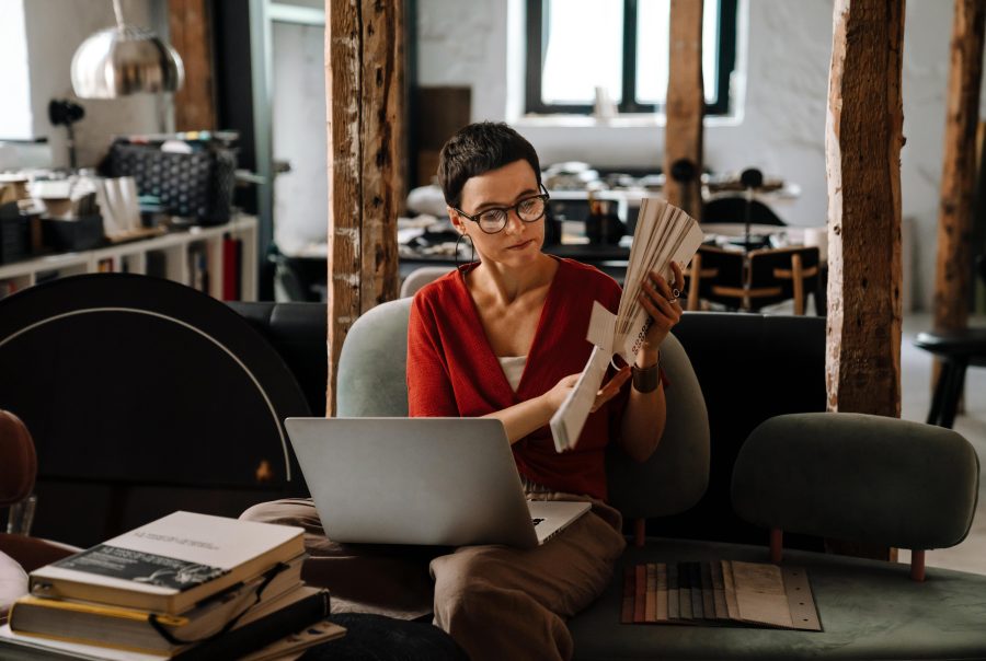 Vrouw bekijkt thuis kleurstalen en documenten aan haar laptop, kleurinspiratie aan huis